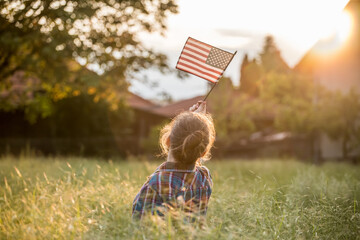 Cute little patriot sitting on the meadow and holding the national flag of United States