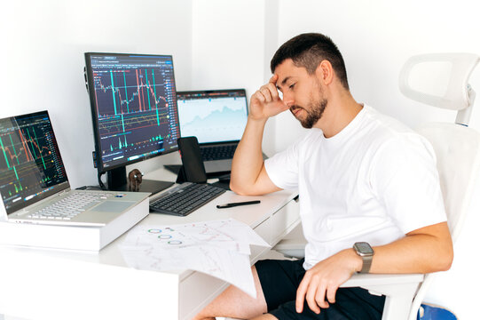 Confident successful busy male trader sitting at desk at home office monitoring stock market looking and analyzing price flow, risks and prospects. Stock trading, cryptocurrency concept