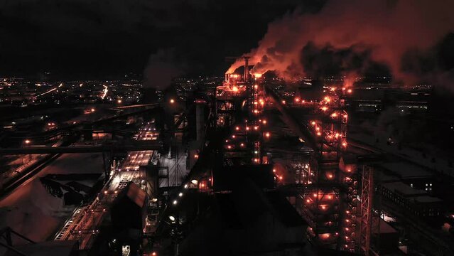 Aerial view of steel plant at night with smokestacks and fire blazing out of the pipe. Industrial panoramic landmark with blast furnance of metallurgical production. Concept of environmental pollution