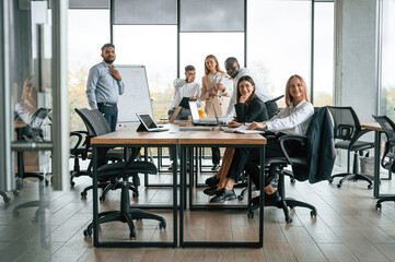By the table and with whiteboard. Group of office workers are together indoors