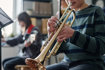 Medium section shot of unrecognizable boy playing trumpet during school orchestra rehearsal in classroom
