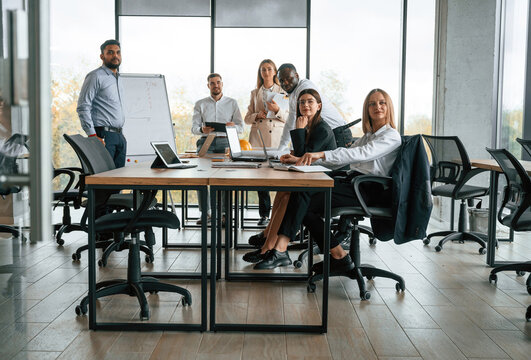 By The Table And With Whiteboard. Group Of Office Workers Are Together Indoors