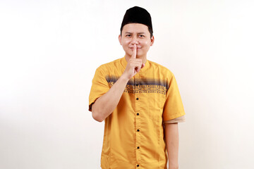 Young asian man wearing typical muslim clothes isolated on white background keeping a secret or asking for silence.