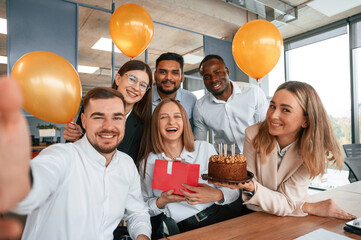 Selfie of happy woman with gift. Employee having a birthday in the office, group of workers