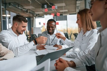 New technology for the project. Talking, sitting by table. Group of office workers are together indoors