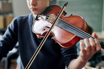 Selective focus crop shot of Caucasian boy practicing violin at music class at school