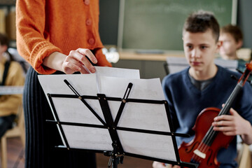 Selective focus shot of unrecognizable female teacher changing sheet music on music stand for boy with violin
