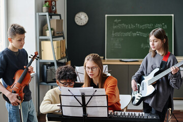 Medium long shot of young music teacher explaining her students how to play part of song during lesson at school © AnnaStills