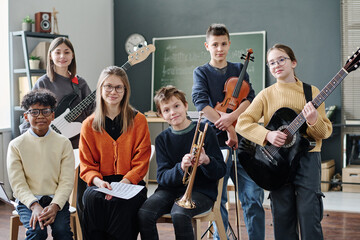 Group of boys and girls taking part in school orchestra and their young music teacher posing for...