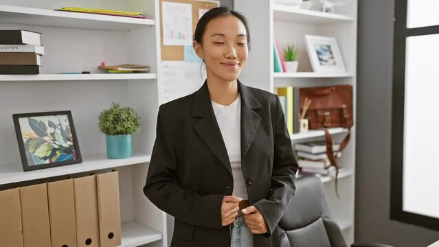 A professional asian woman in a blazer stands confidently in an office, personifying career-focused elegance.