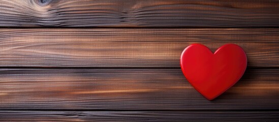A red heart sits prominently on a textured wooden background, creating a warm and rustic aesthetic. The heart symbolizes love and affection, perfect for Valentines Day celebrations.