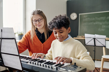 Medium shot of African American teen boy playing electronic piano at music class, his young...