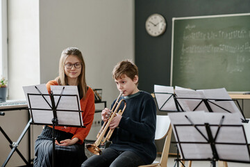 Young Caucasian female music teacher listening to middle school student playing trumpet during class - Powered by Adobe