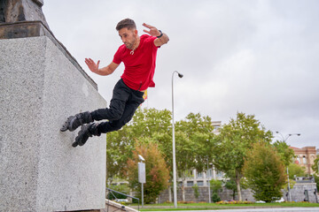 young man skating on inline skates jumping over city wall