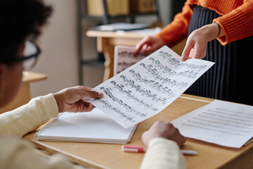 Selective focus medium closeup of unrecognizable teacher giving sheet music to student