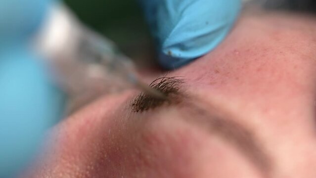 Micro blading tattoo , permanent make-up. The master in gloves, using a special needle, injects pigment into the skin and colours the eyebrows with the hair technique, close-up view
