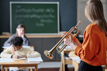 Selective focus shot of unrecognizable young female music teacher holding trumpet conducting lesson