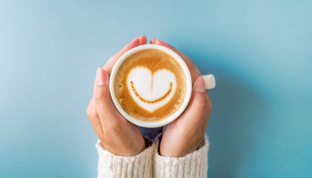 Hands holding a cup of coffee with a happy face and heart emoji, blue background, copy space

