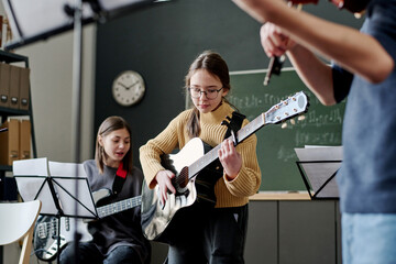 Selective focus shot of girl and her classmates playing instrumental music in classroom at school