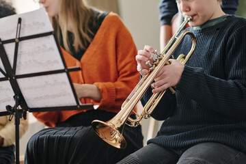 Selective focus crop shot of boy playing in school orchestra practicing trumpet during rehearsal