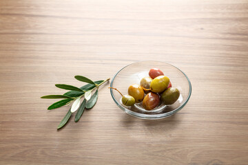 Olives in a plate with bunch of leaves on wooden table
