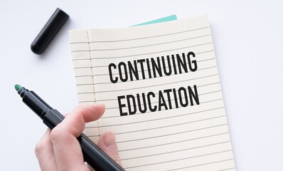 Black marker in hand over open notebook with Continuing Education text