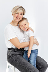 A young woman and a boy are hugging and smiling. Mom holds her 4-year-old son on her lap. Love and tenderness. White background. Vertical.