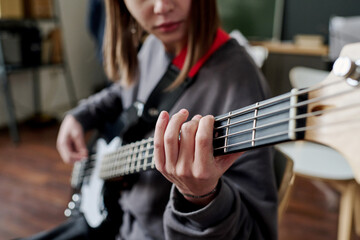 Selective focus shot of Caucasian teen girl sitting in classroom playing bass guitar at music class
