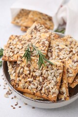 Cereal crackers with flax, sunflower, sesame seeds and rosemary in bowl on light table, closeup
