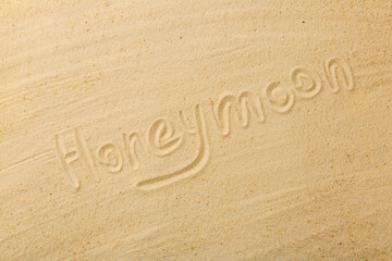 Word Honeymoon written on sand, top view