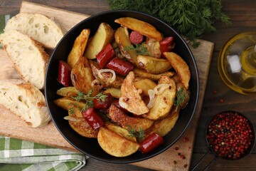 Delicious baked potato with thin dry smoked sausages in bowl, bread and spices on wooden table, flat lay