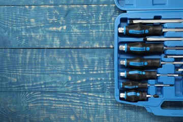 Set of screwdrivers in open toolbox on blue wooden table, top view. Space for text