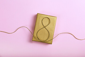 Golden jute twine in the shape of eight as symbol of symbol of women's equality on a present for international women's day. Close up, copy space for text, background.