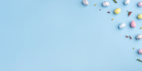 Festive Easter background. Multicoloured Easter eggs and flowers on a blue table. Banner with a...