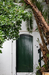 Green wooden slatted door with handle in white wall. Entrance to a hotel building surrounded by...