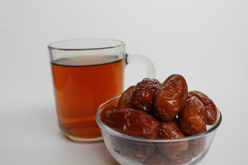 Deglet noor or deglet nour or date palm or dates, in a transparent bowl, with a glass of tea, isolated on white background