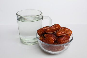 Deglet noor or deglet nour or date palm or dates, in a transparent bowl, with a glass of water, isolated on white background
