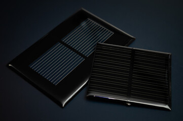 Shot of two photovoltaic solar panels, placed on a dark surface with a subtle light reflecting upon...
