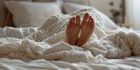 Fototapeta na wymiar Feet under a white blanket, in bed, in a comfortable apartment, concept of Cozy atmosphere