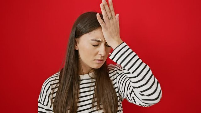 Young beautiful hispanic woman wearing stripes t shirt standing surprised with hand on head for mistake, remember error. forgot, bad memory concept. over isolated red background
