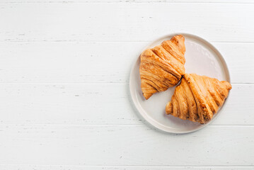 Plate with two fresh croissants on white wooden table. Top view.