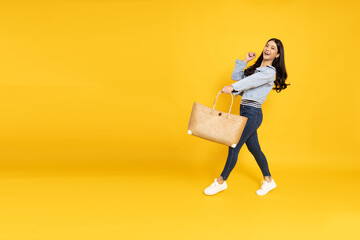 Young Asian woman walking and holding bags isolated on yellow background, Shopper or shopaholic concept