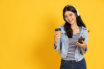 Young Asian woman listening favourite music on mobile phone application with wireless headphones and dancing isolated on yellow background - 747377903