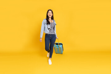 Happy Young Asian traveler woman dragging blue suitcase bag isolated on yellow background, Tourist...