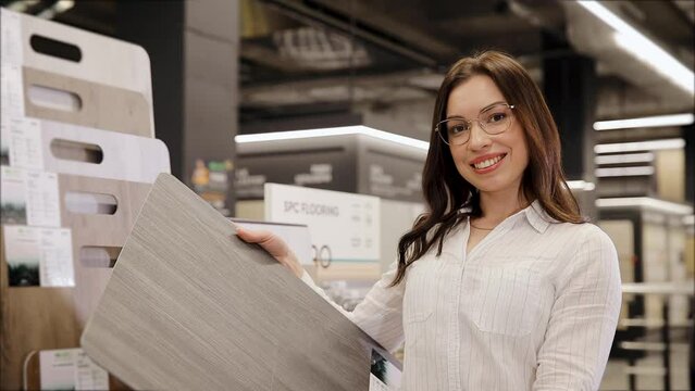 Woman holding parquet board panel sample. SPC flooring. Young woman examines a laminate floor in a hardware store. Close-up