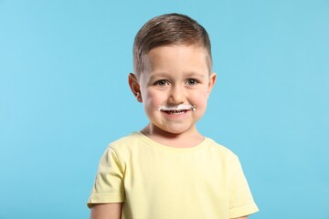 Cute boy with milk mustache on light blue background