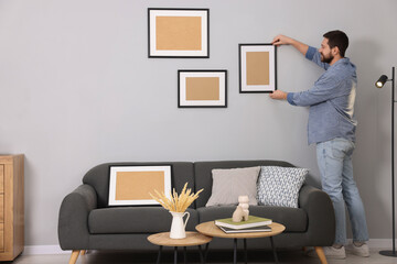Man hanging picture frame on gray wall at home