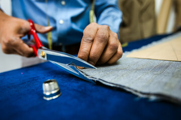 Young African American tailor cuts with scissors fabric in his own atelier.