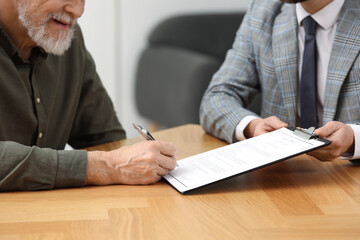 Notary showing senior man where to sign Last Will and Testament at wooden table indoors, closeup