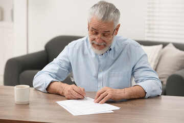 Senior man signing Last Will and Testament at wooden table indoors